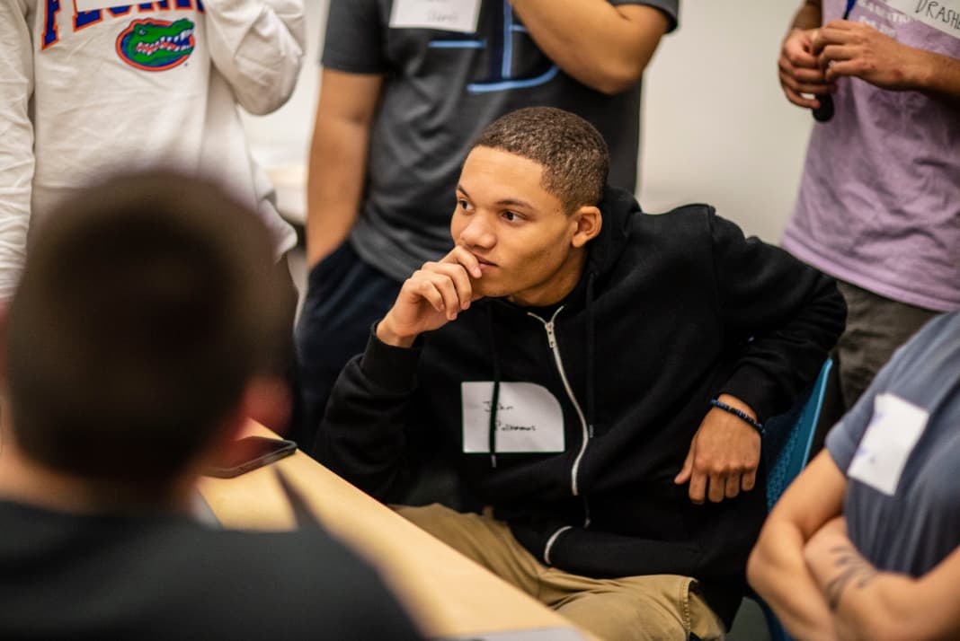 A student sitting in a classroom surrounded by classmates.