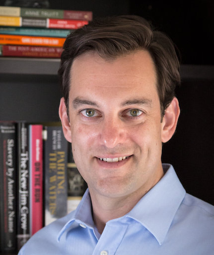 Lance Gravlee in front of a bookshelf smiling