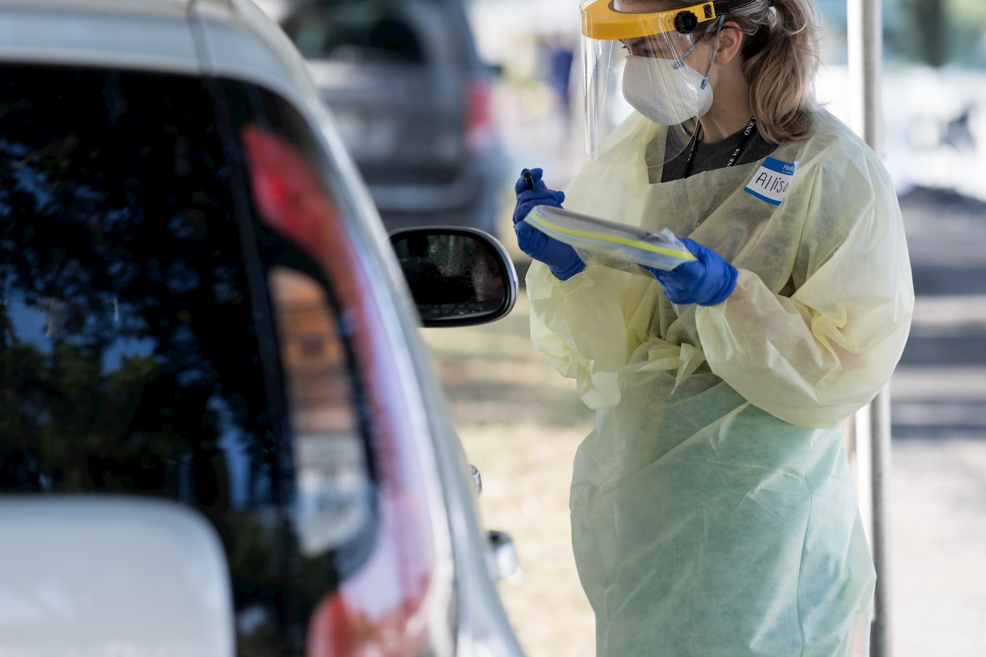 A medical professional assists someone in a drive-through COVID-testing site.