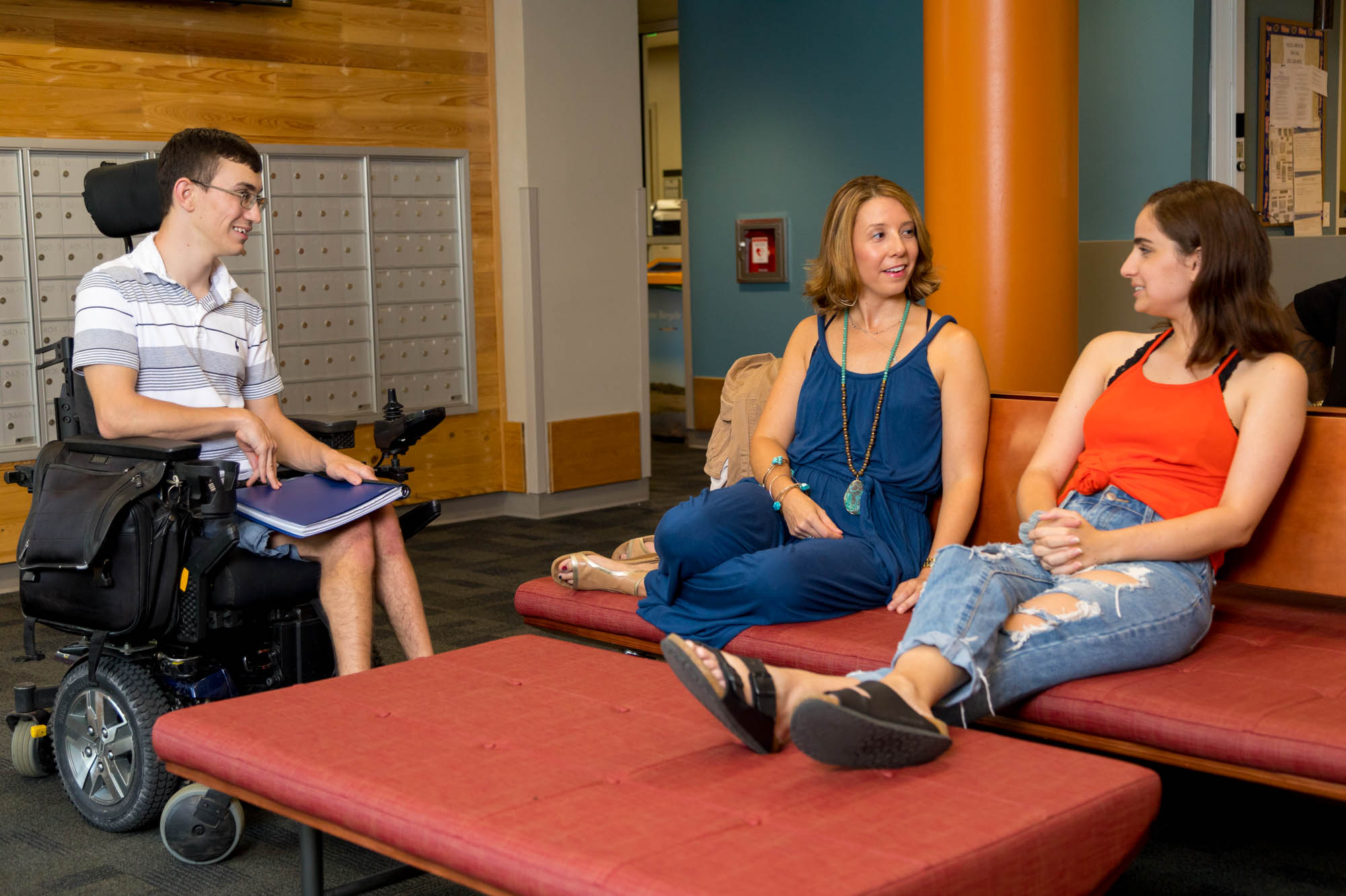 Three people sit around a table, two are sitting on a couch and one is using a wheelchair