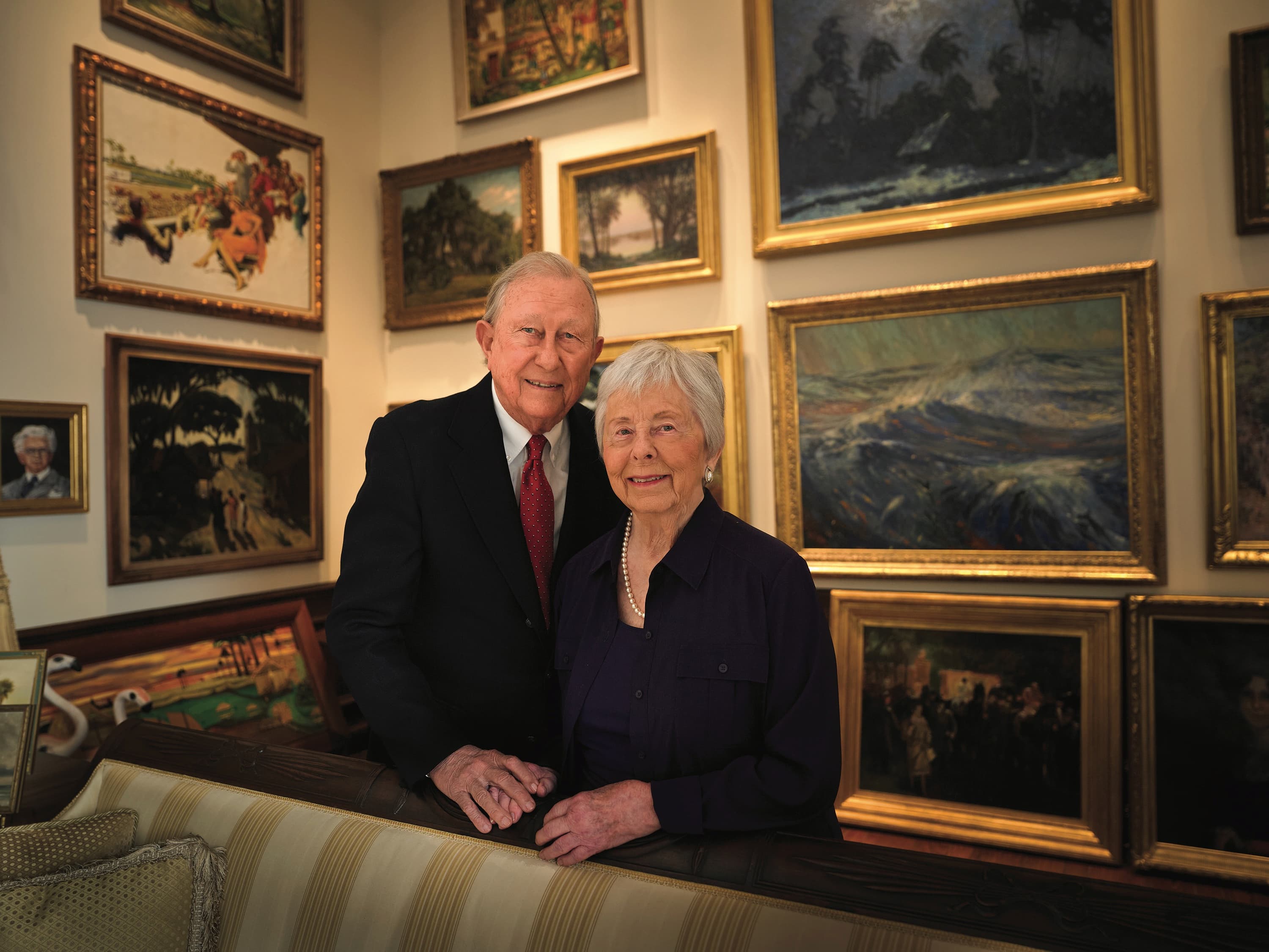 A portrait of Sam and Robbie Vickers in front of a gallery wall in their home. The Vickers donated a large collection of Florida paintings to the Harn Museum.