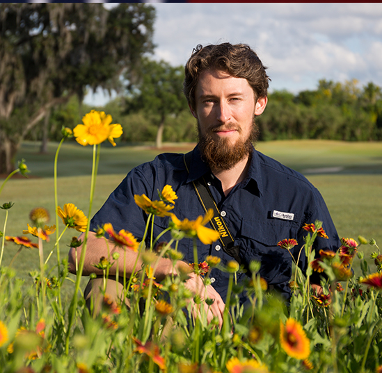 Adam Dale poses in front of Florida wildflowers