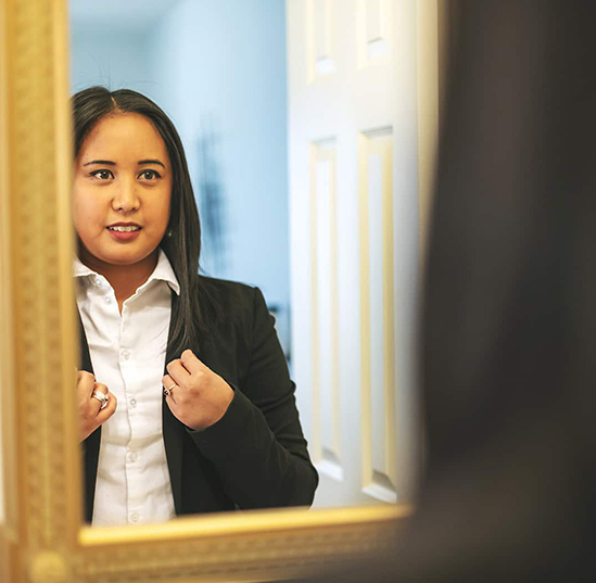 A woman adjusts her jacket in her reflection in a mirror 