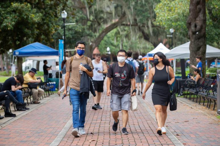 Three students wearing protective face masks walk along the University of Florida campus. 