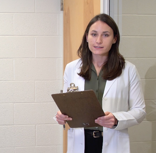 A dietician in a white coat holds a clipboard while speaking.