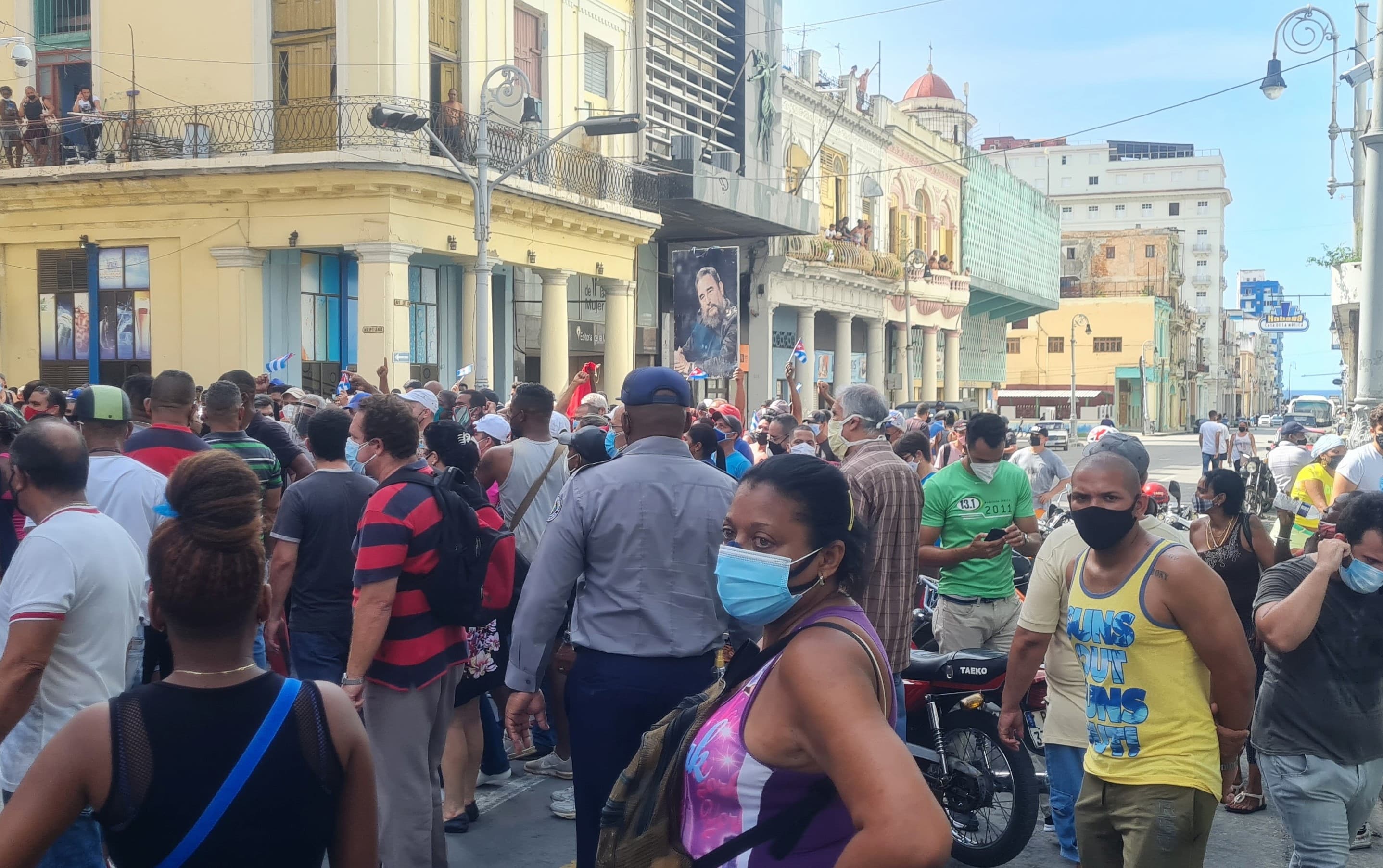 A group of protesters, some in masks, gather in an outdoor intersection in Cuba
