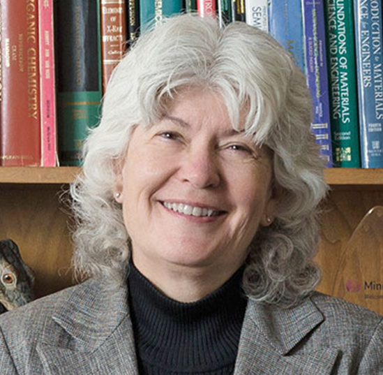 Cammy Abernathy, dean of the Herbert Wertheim College of Engineering at the University of Florida, smiles as she poses for a professional photo in front of a full bookcase