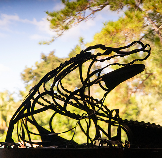 A steel sculpture of an alligator is silhouetted against a bright blue Florida sky 