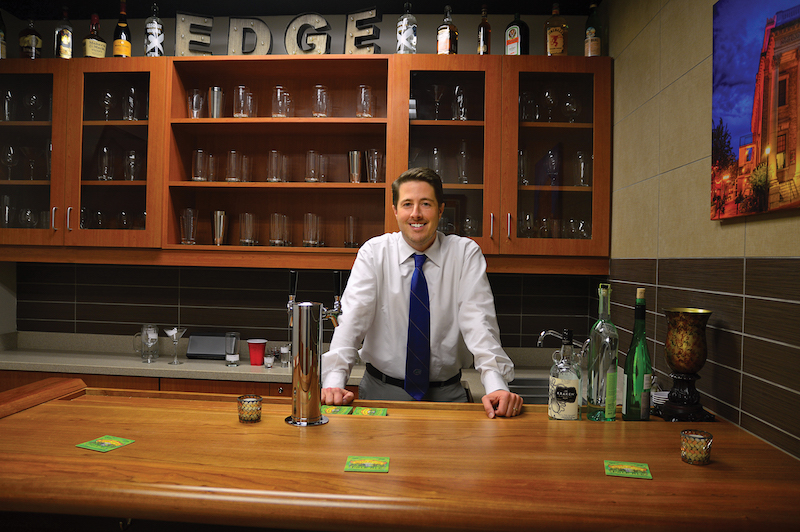 Professor Robert Leeman in the bar lab at UF. He leans on a wooden bar top with drinkware behind him and beer taps next to him.