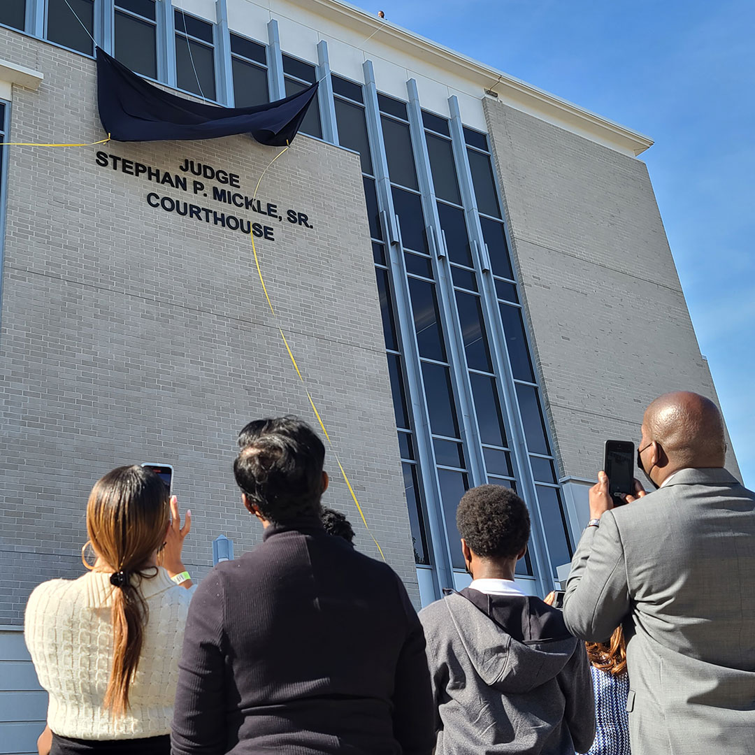 Several people stand as a curtain is lifted revealing the new name of the Alachua County Courthouse as the Judge Stephan P . Mickle, Sr., Courthouse