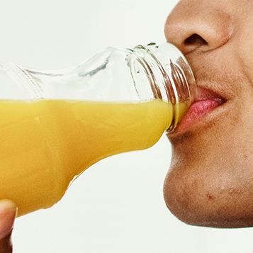 Image shows person drinking orange juice from glass jar. 