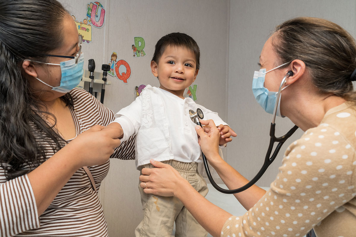 Nurse using stethoscope on young boy while mother watches