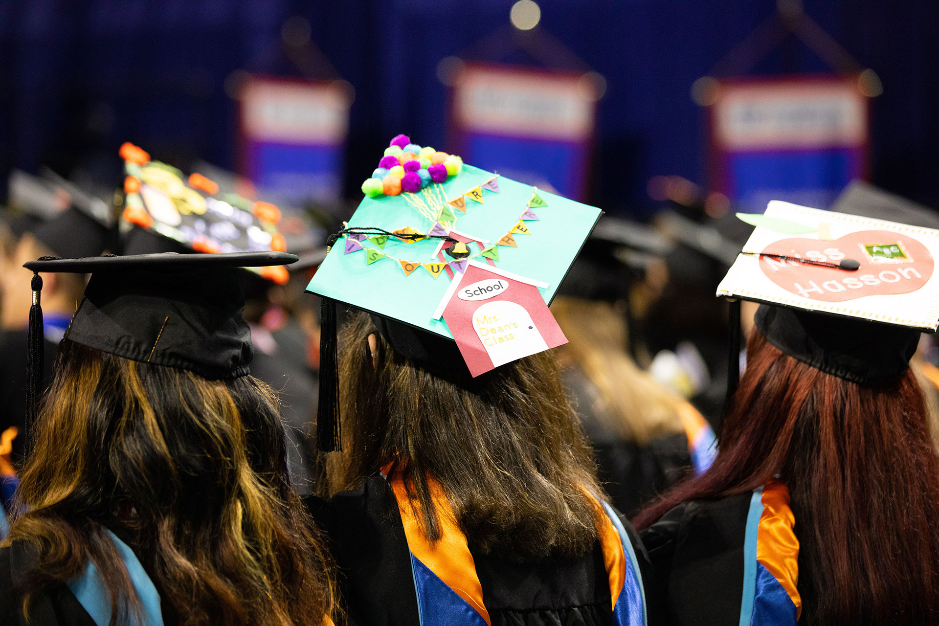 A photo from the back of three students in caps and gowns at commencement.