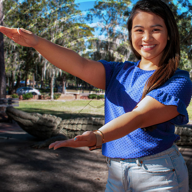 A young woman holds her arms open, motioning UF's gator chomp