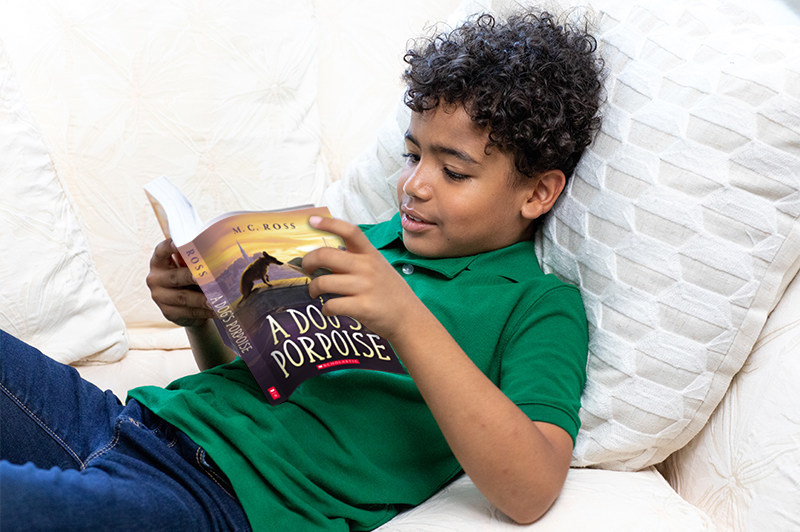 A boy lays on a pillow while reading a book