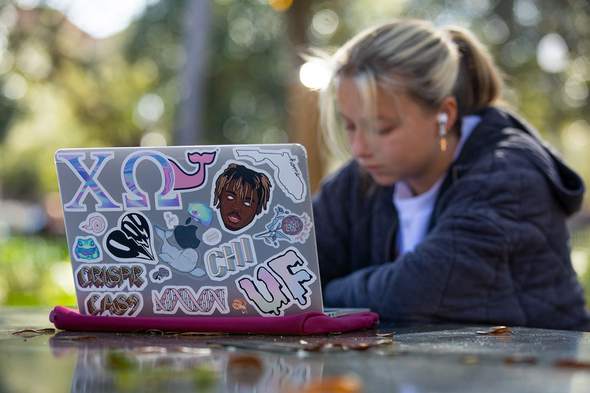 Focal point: a laptop with over a dozen stickers. A student works in the background.