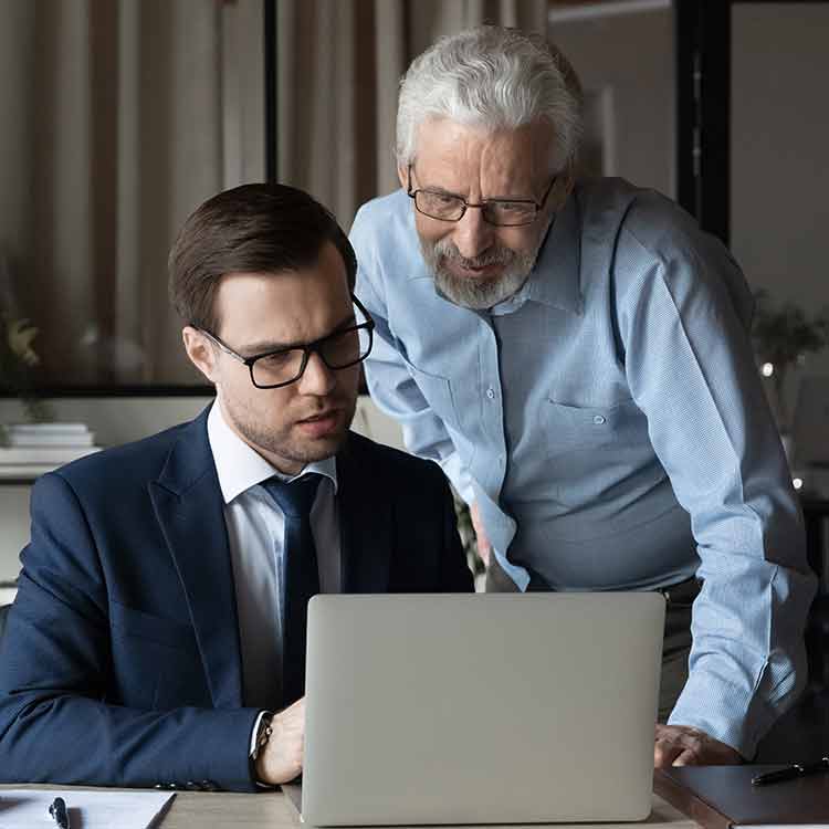 Two men look at a laptop screen. 