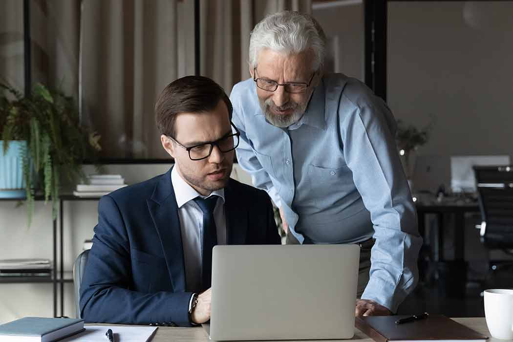 Two men look at a laptop screen. 