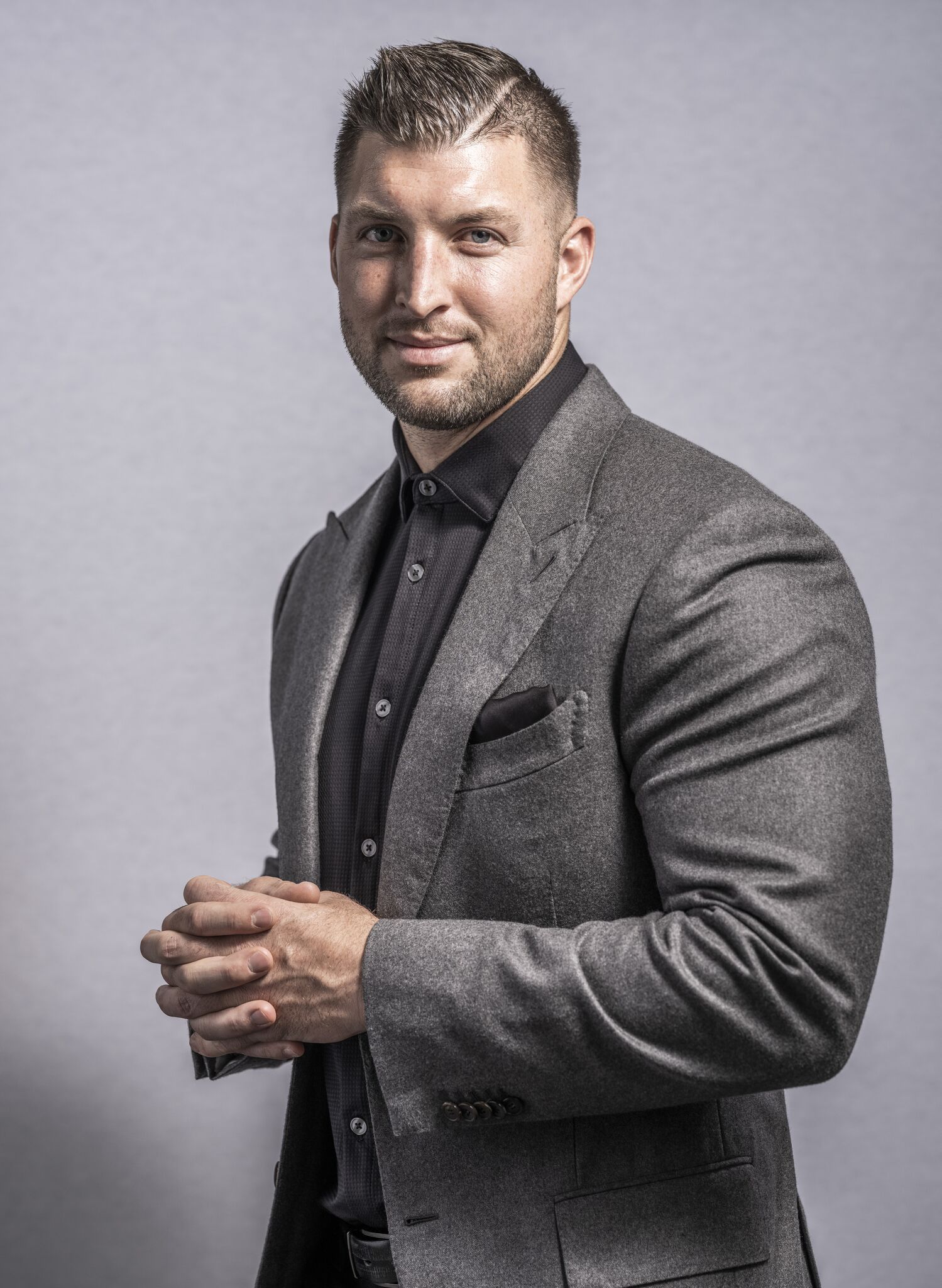 A headshot of a man with his hands together in a gray suit.