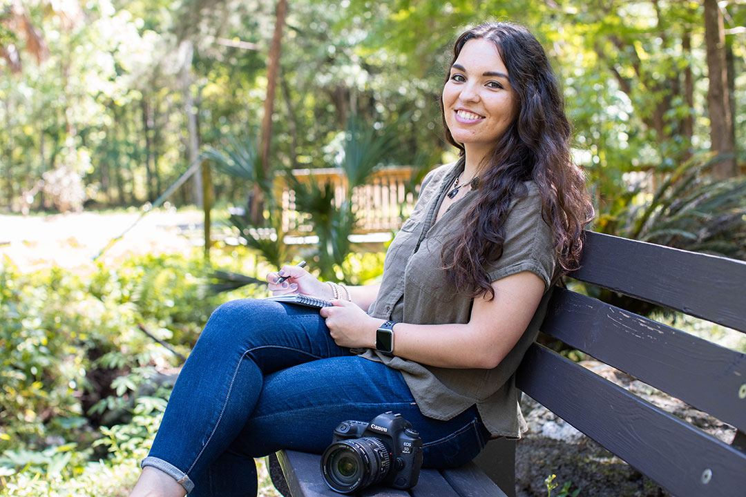 A woman sits on a bench with a camera by her side. 