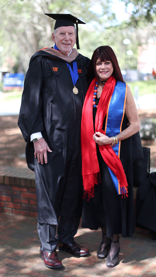 A man in graduation regalia standing next to a woman outside.