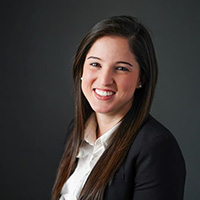 A headshot of a woman in a white shirt and black jacket.