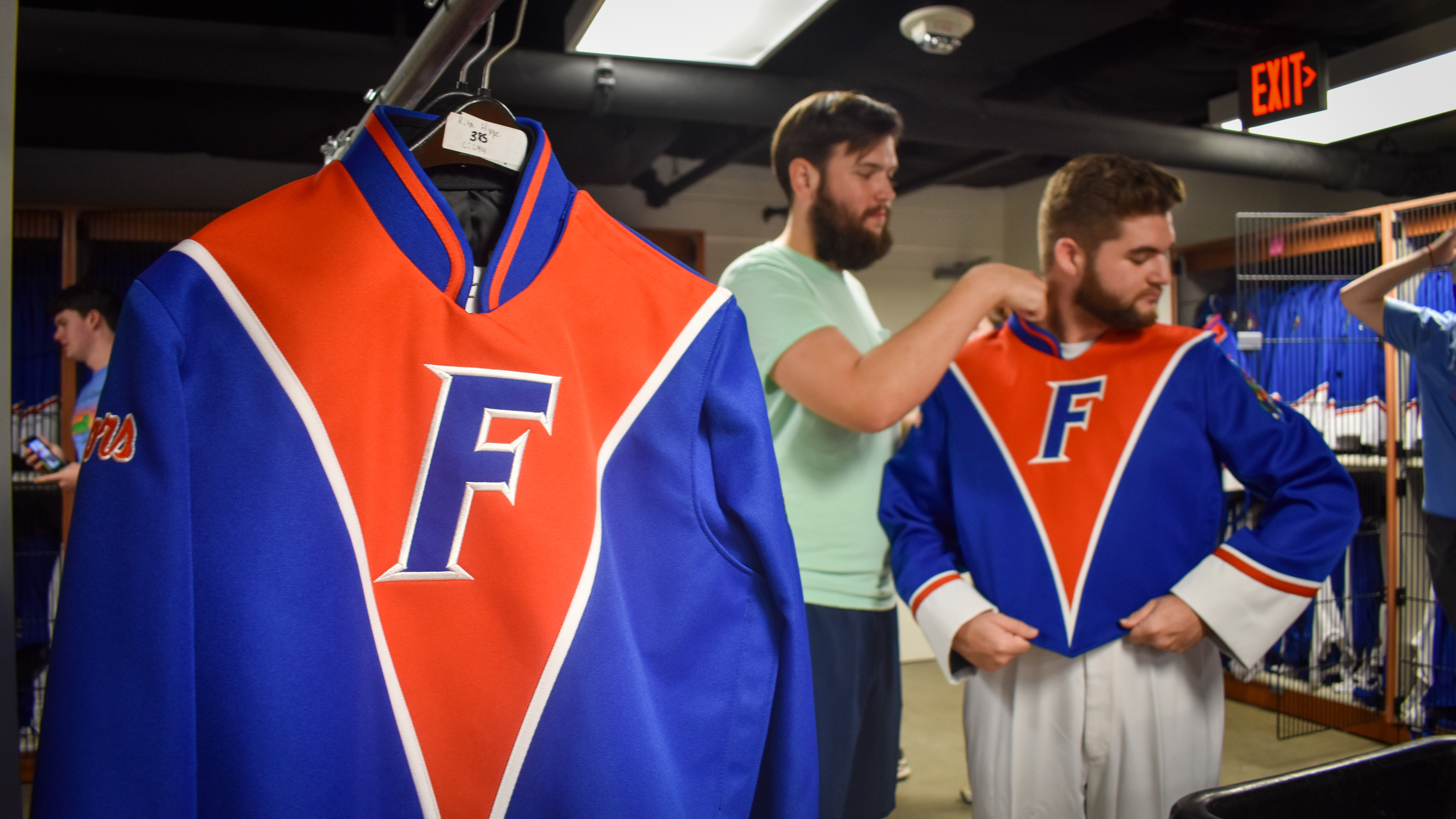 A student sizes another student for a marching band jacket with another marching band jacket in the foreground.