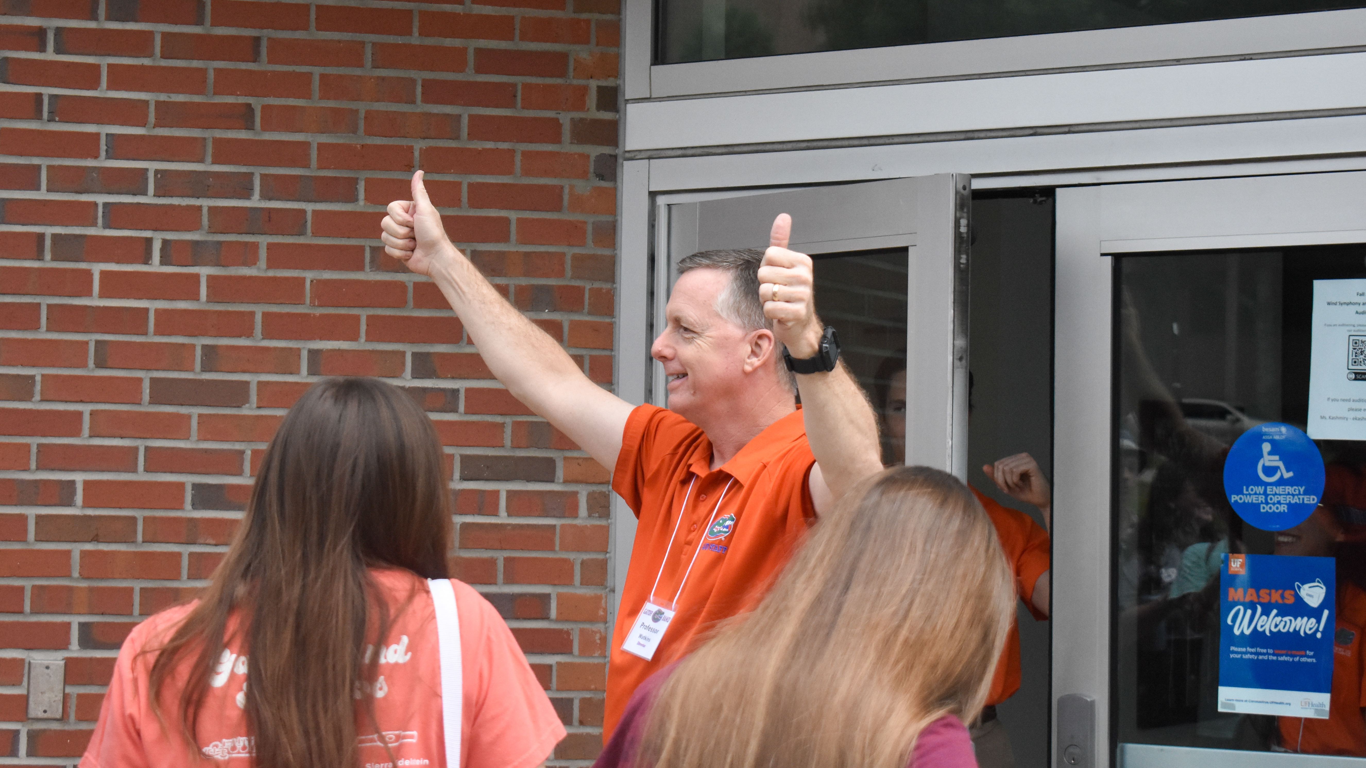 A man in an orange polo holds two thumbs up.