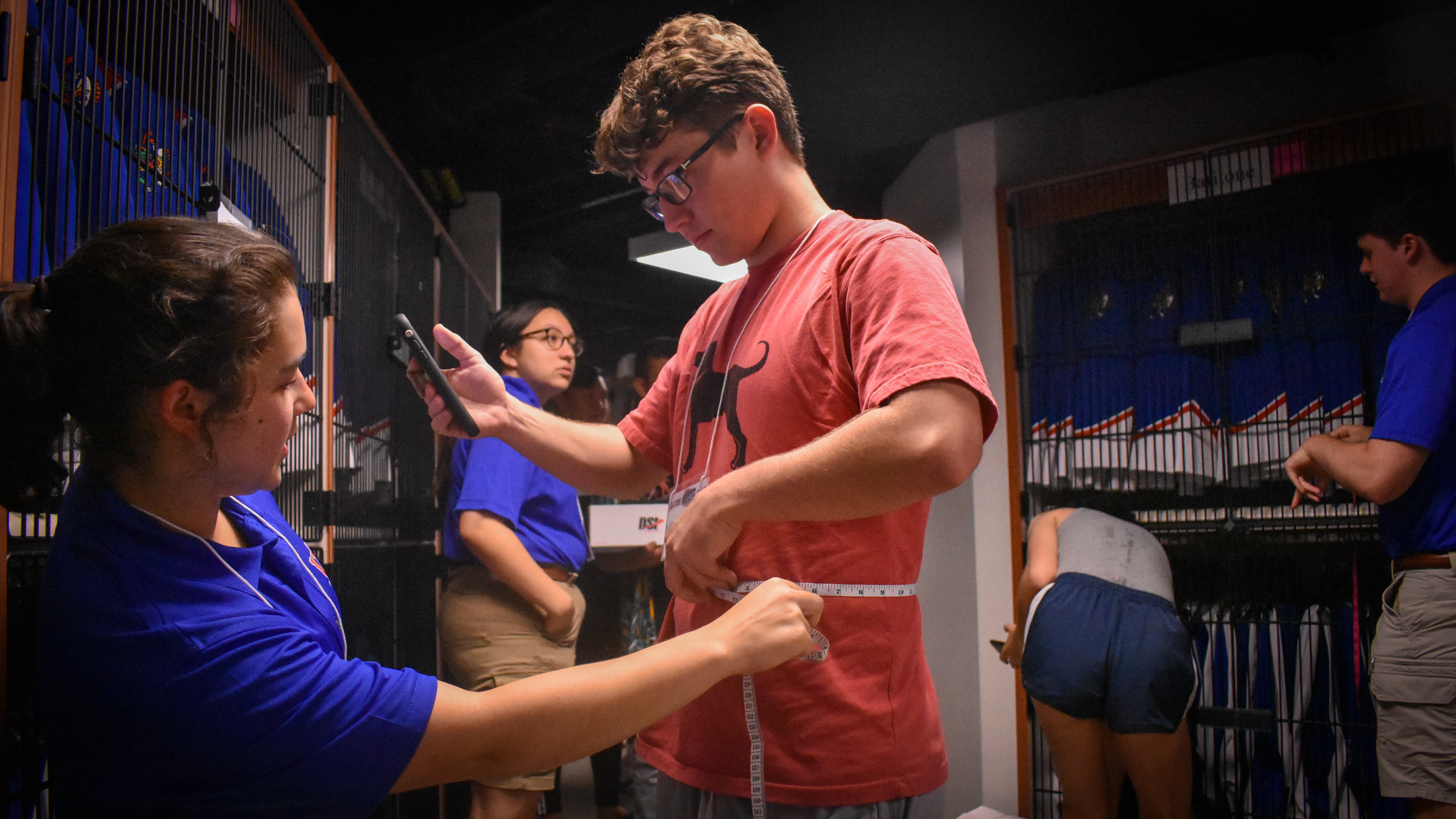 A student holds a measuring tape around his waist while another student reads the measurement.