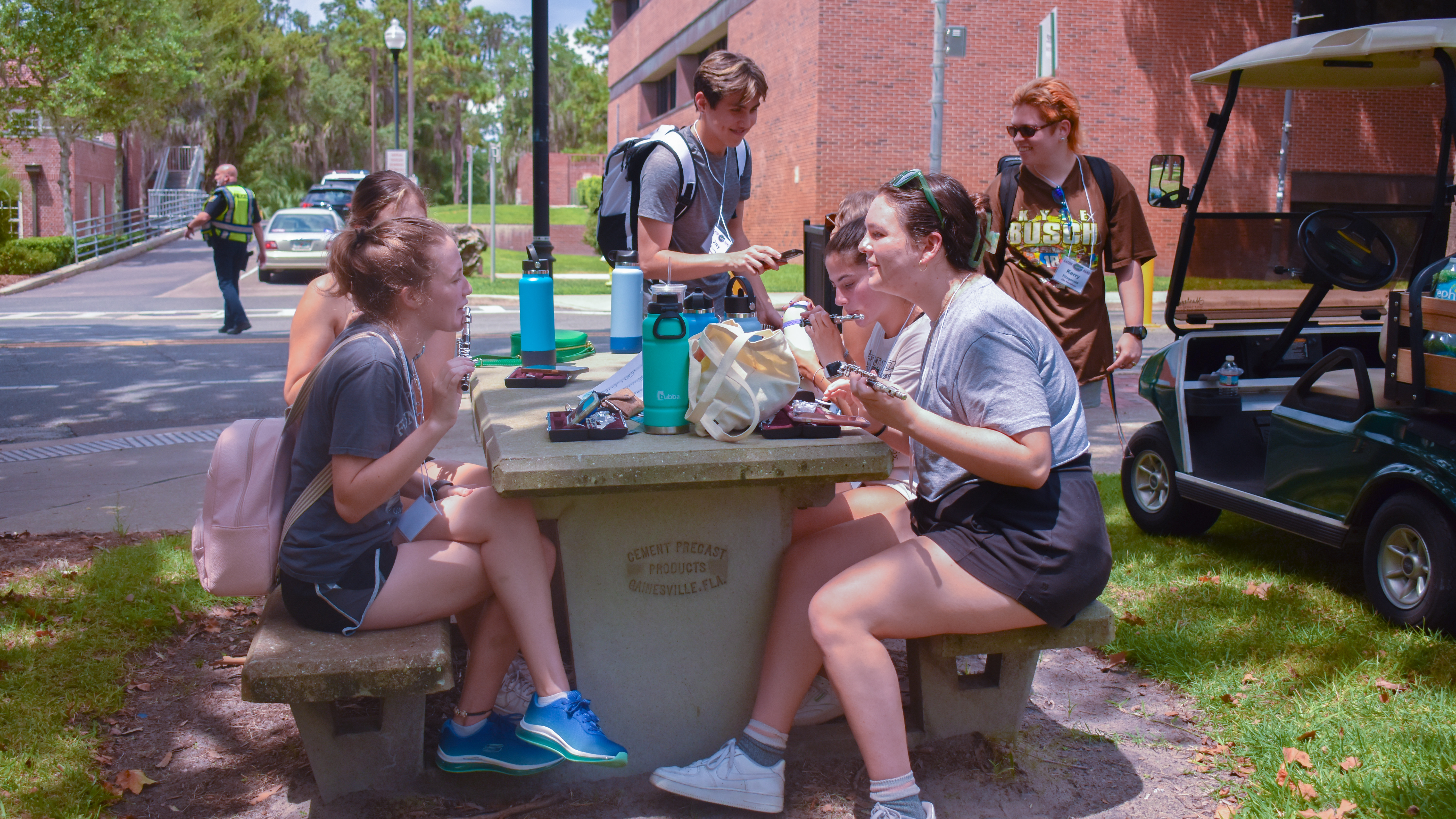 Students sit around a picnic table playing piccolos. 