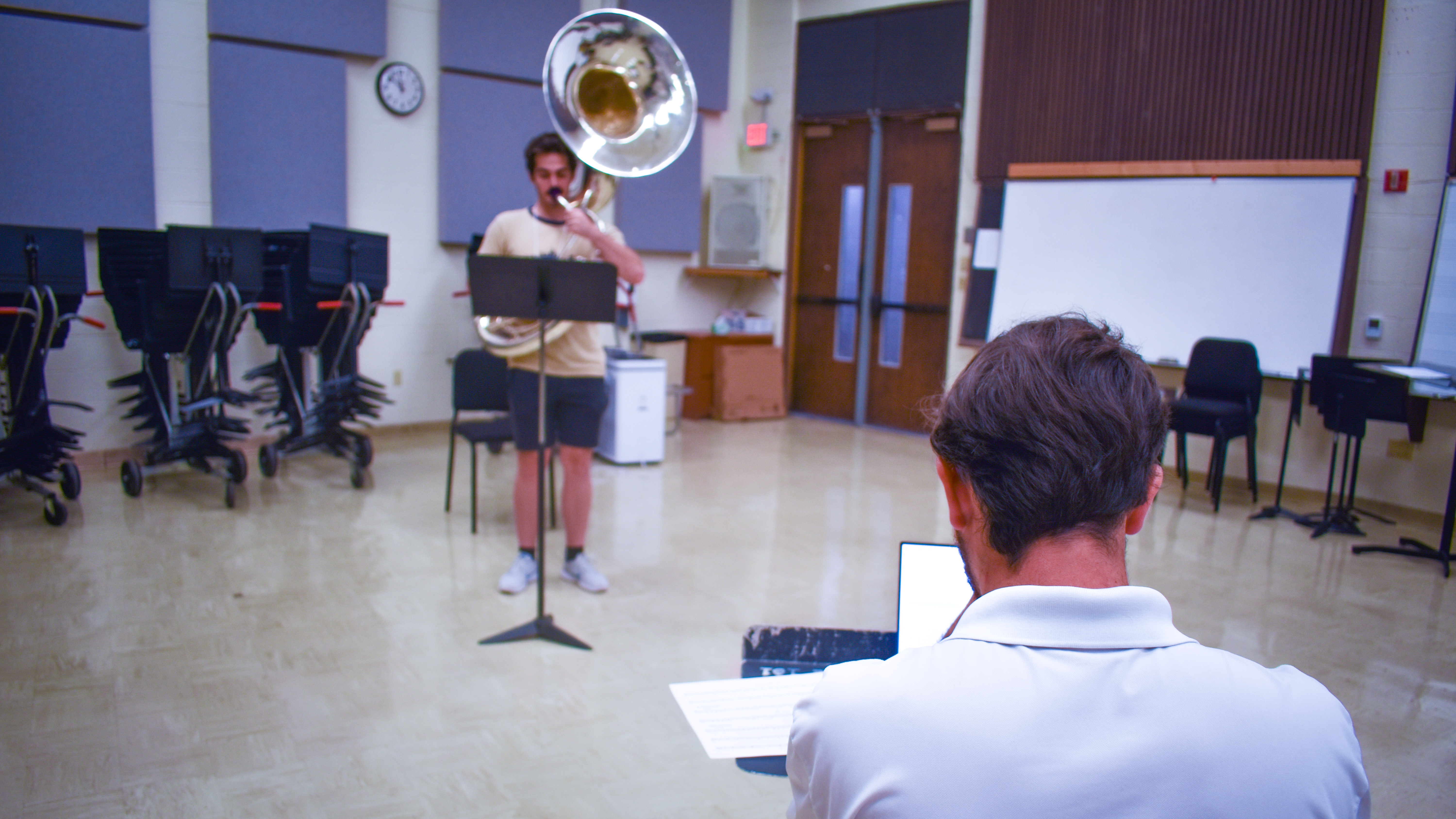 A student auditions on a sousaphone with an instructor grading on a laptop.