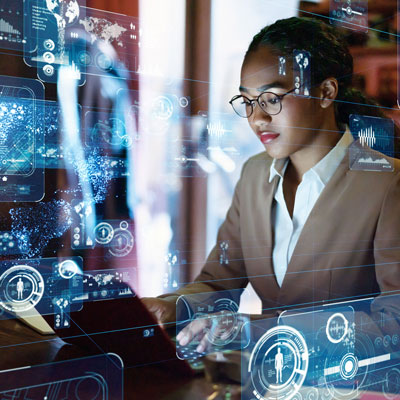 A woman in a suit works on a computer with digital graphics surrounding her. 