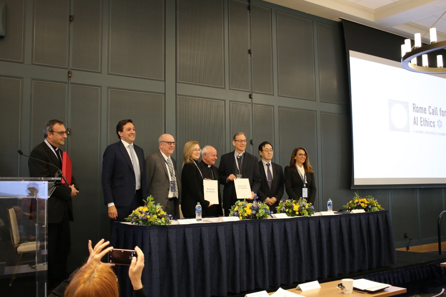 A group of people stand behind a table on stage.