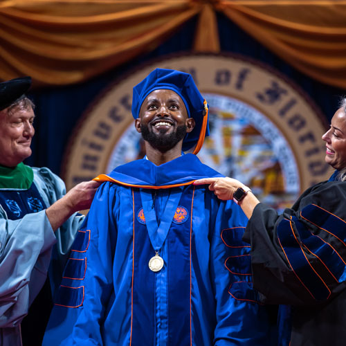 A person in graduation regalia receives his doctoral hood. 