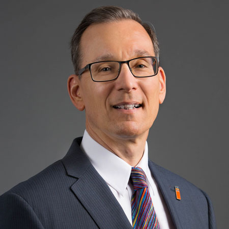 A headshot of UF Provost Joseph Glover in a suit with a gray background. 