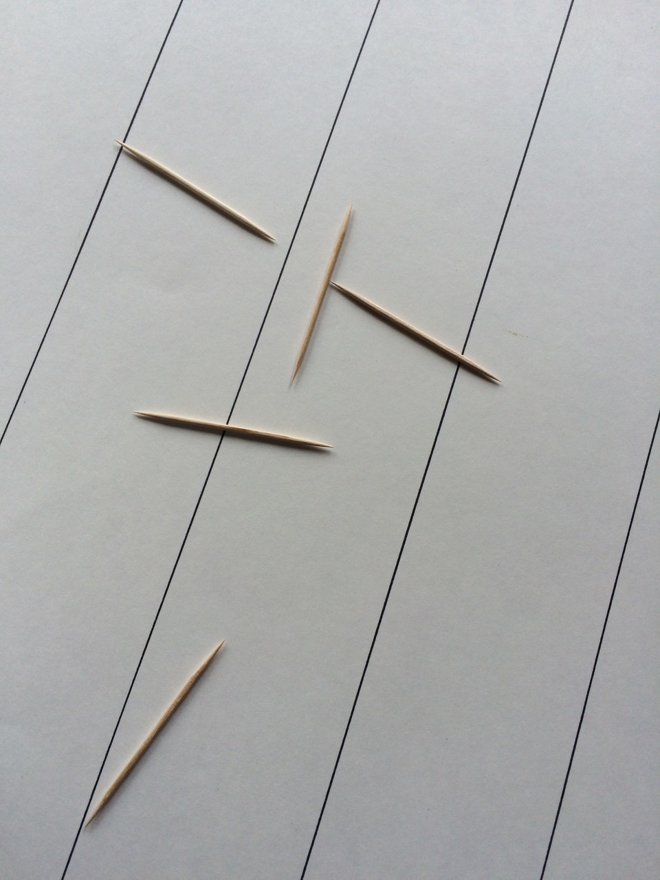 Five toothpicks scattered on a piece of paper with parallel lines drawn across it. Some of the toothpicks cross those lines.
