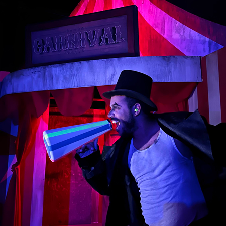 A student dressed as a ringleader poses in front of a haunted house.