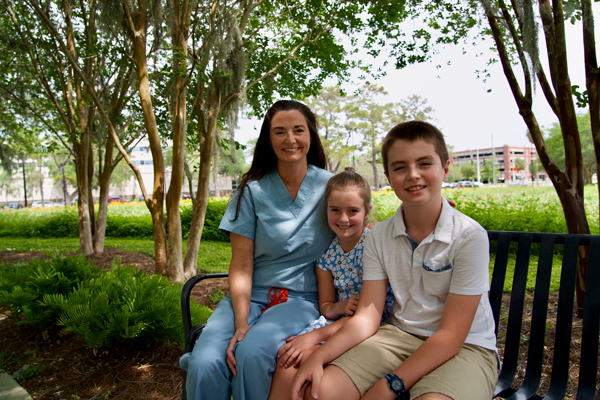 A doctor in scrubs sits on a bench with her two children.