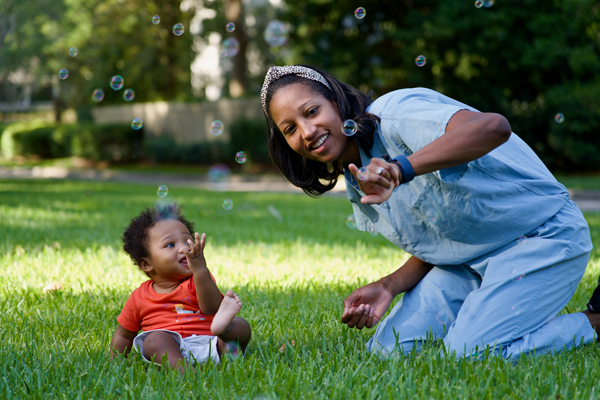 A doctor in scrubs plays with bubbles with her baby.