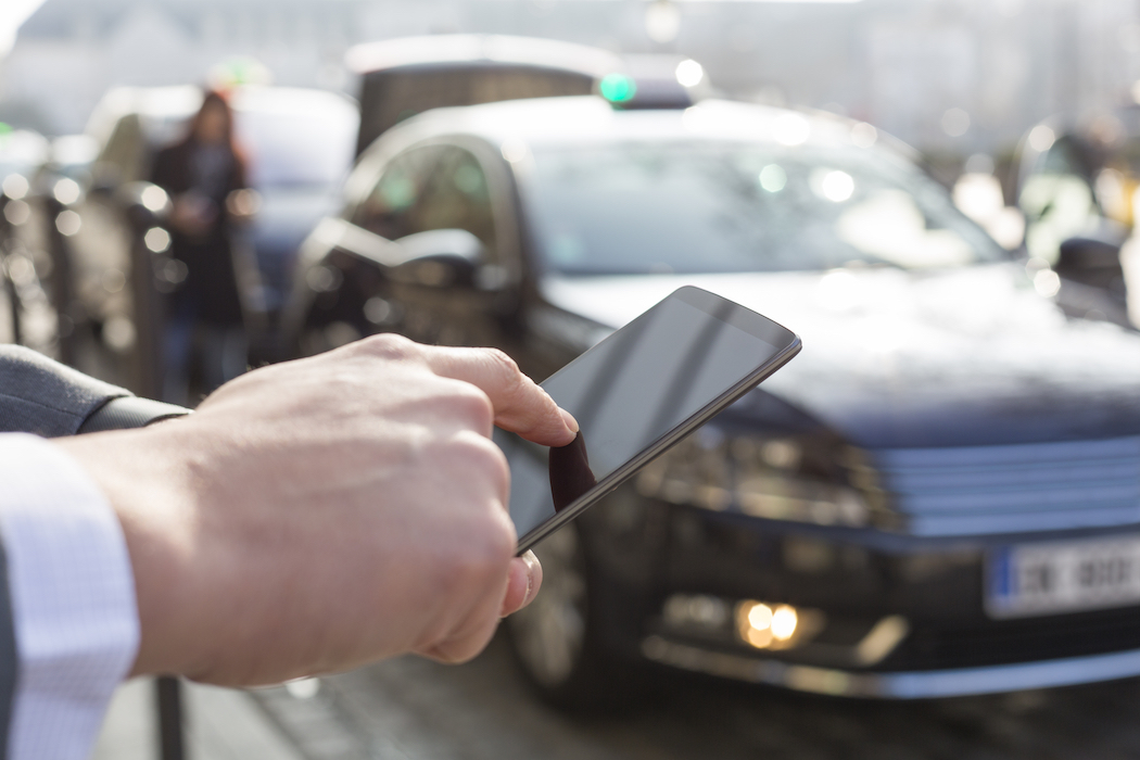 A man's hand holds a smartphone to select an option while a taxi cab waits in the background