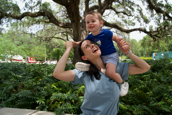 A doctor in scrubs carries her child on her shoulders.