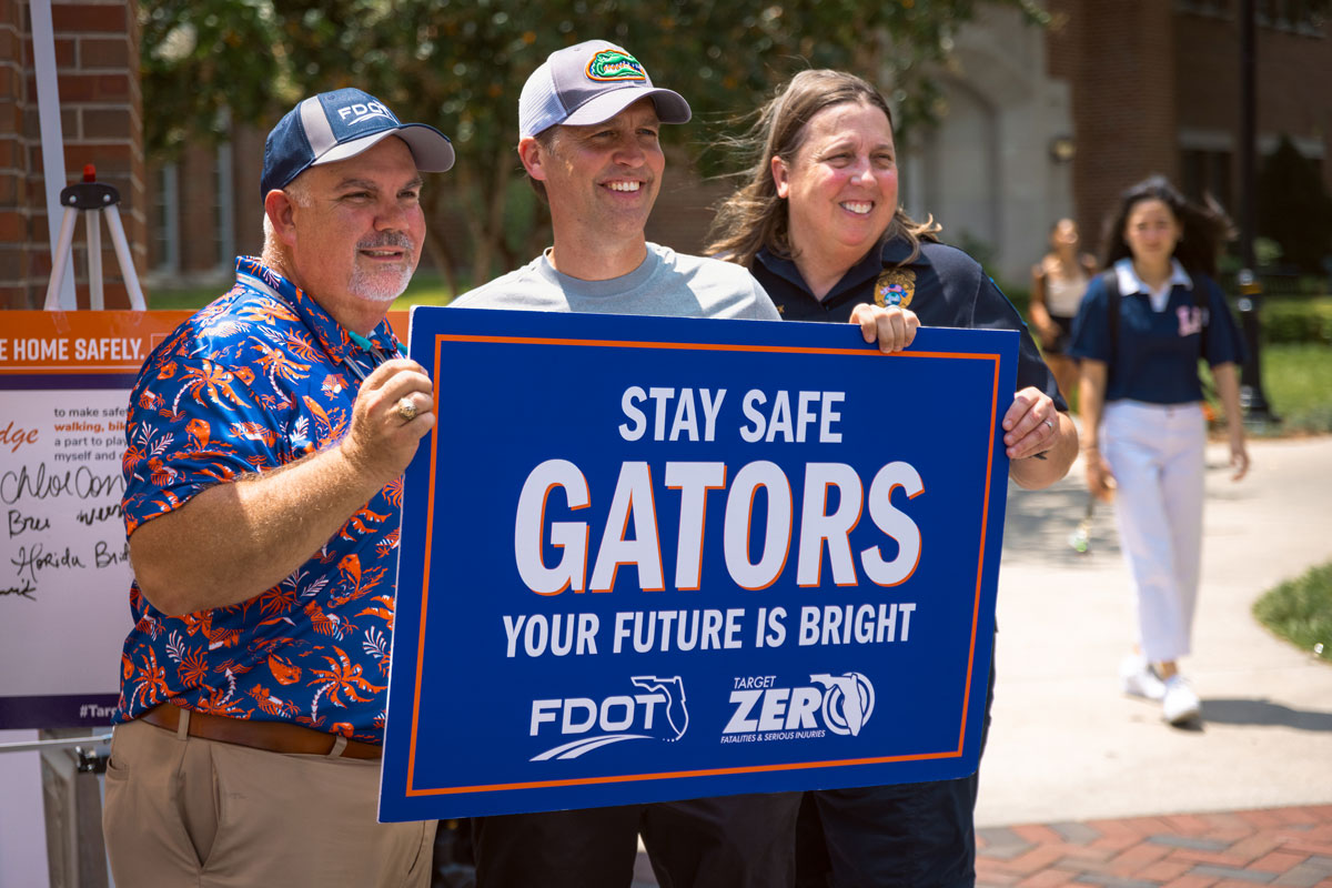 Three individuals stand together holding up a sign for pedestrian and bicyclist safety.