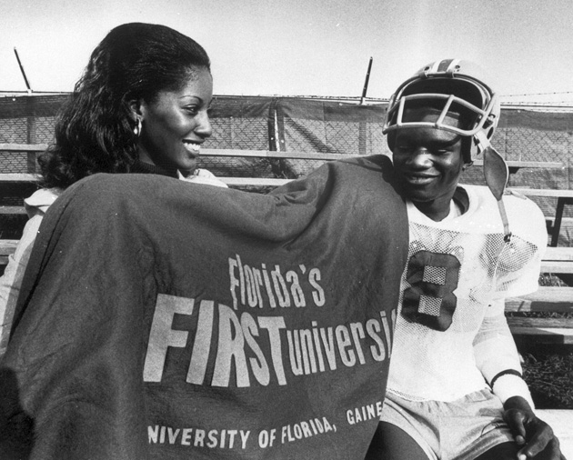 Cynthia Mays, the University of Florida's first Black homecoming queen, poses holding a shirt next to a football player.