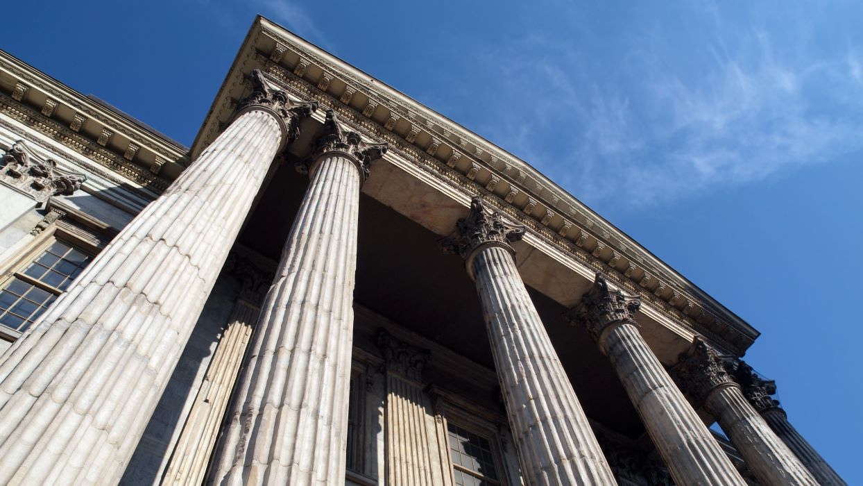 Looking up a steep angle at the ornate columns of a stone bank building with a blue sky above