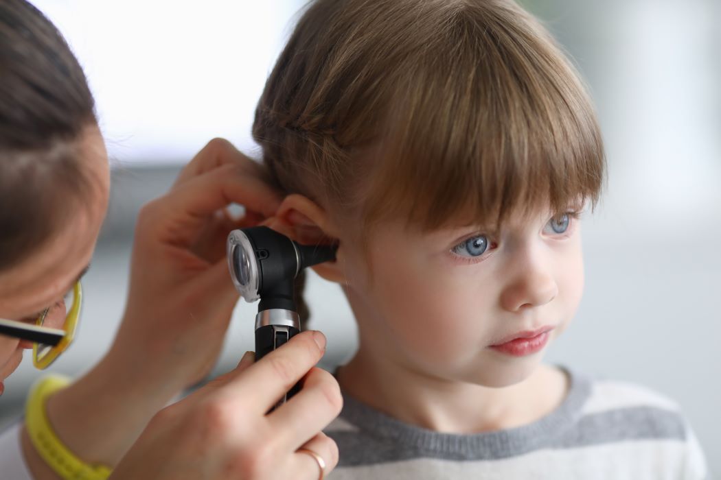 A young child faces forward as a doctor's hand is seen inserting a scope into their ear canal
