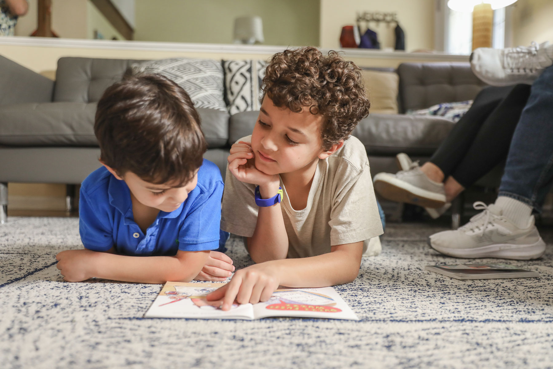Two young children laying and reading a book together on the floor