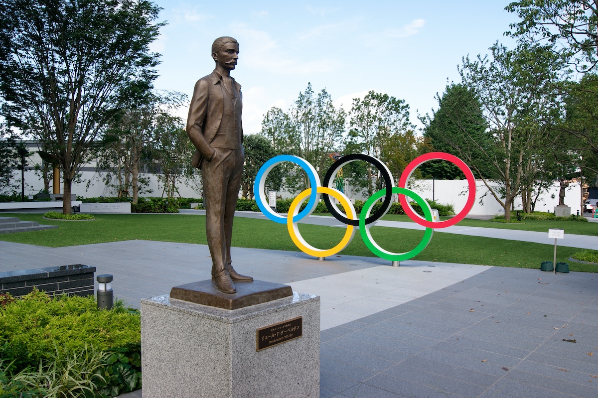 A statue of the father of modern olympics with the rings in background