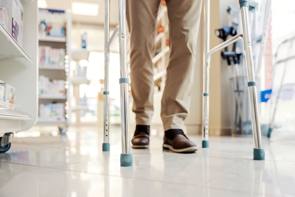 A view of a man's legs as he uses a walker to walk down a hallway in a hospital