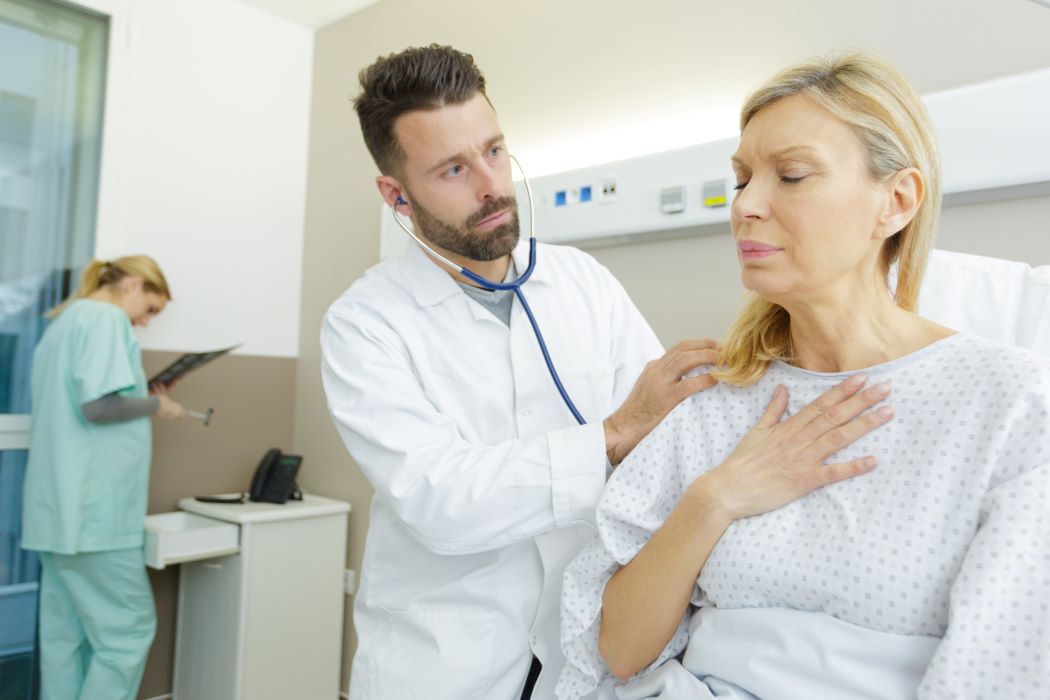 A woman in a hospital gown clutches her chest in pain while a doctor comforts her