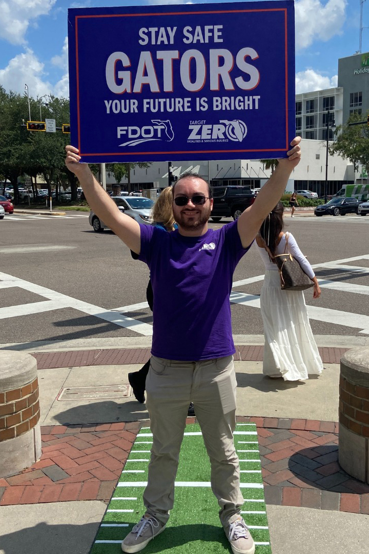 A man holds a sign while standing at the corner of a street intersection.